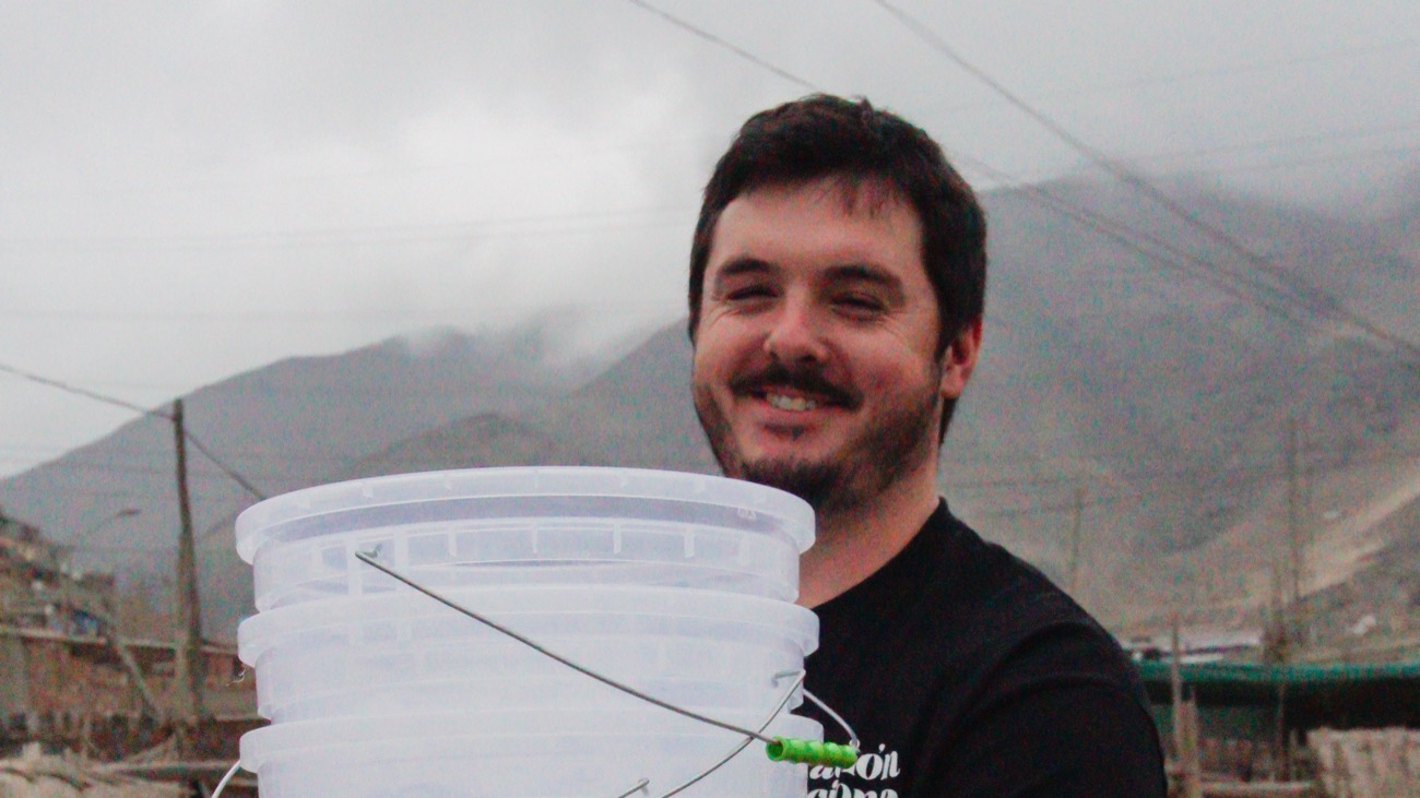 A team member smiling as he carries a new water filter bucket to a family